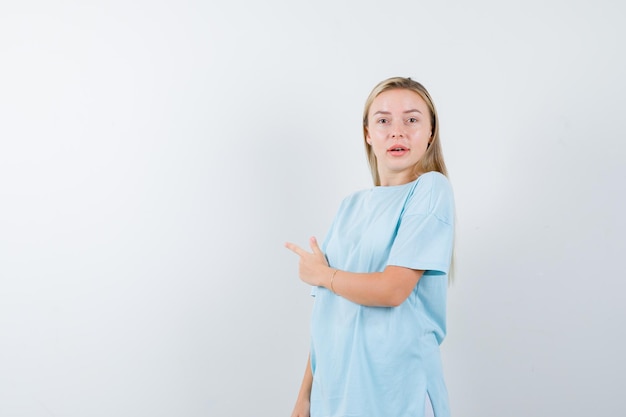 Mujer rubia en camiseta azul apuntando a la izquierda con el dedo índice y mirando sorprendido