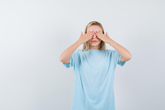Mujer rubia en camiseta azul cubriendo los ojos con las manos y mirando seria