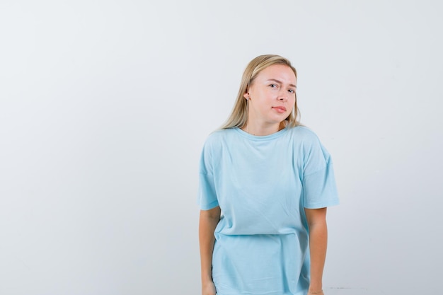 Mujer rubia en camiseta azul de pie derecho y posando a la cámara y mirando lindo