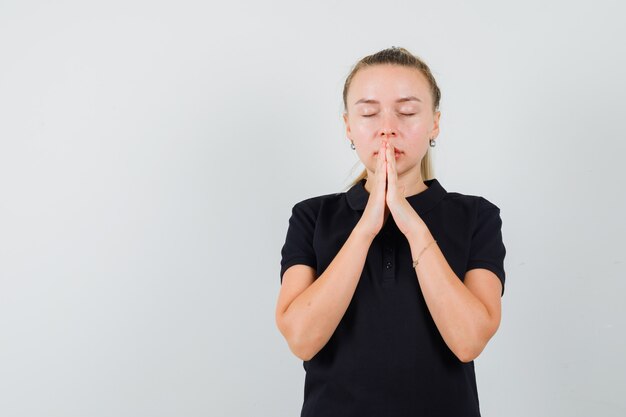 Mujer rubia en camiseta negra rezando y cerrando los ojos y mirando relajado
