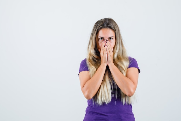 mujer rubia en camiseta violeta juntando las manos en la cara y mirando esperanzada, vista frontal.