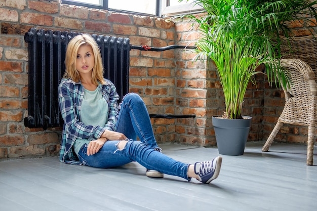 Mujer rubia casual en jeans de mezclilla posando en el piso de la sala de estar.