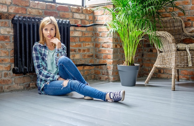 Mujer rubia casual en jeans de mezclilla posando en el piso de la sala de estar.