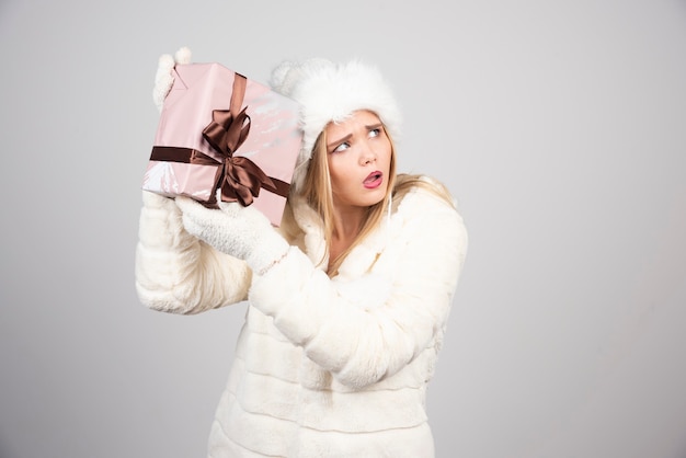 Mujer rubia en chaqueta blanca con caja de regalo.