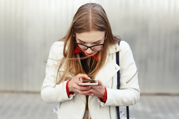 Mujer rubia con chaqueta blanca toma una foto en su teléfono