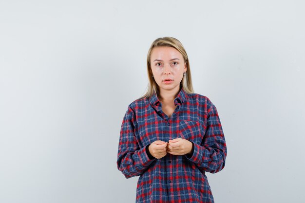 Mujer rubia cogidos de la mano mientras toca la consola en camisa a cuadros y mirando enfocado, vista frontal.