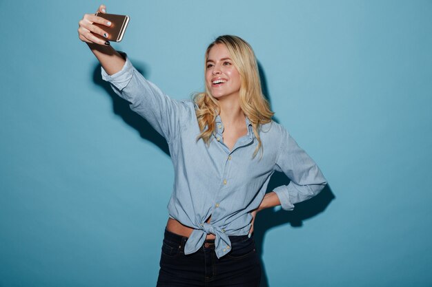 Mujer rubia complacida en camisa haciendo selfie en smartphone