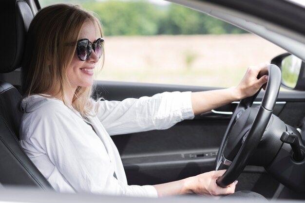 Mujer rubia conduciendo un automóvil con gafas