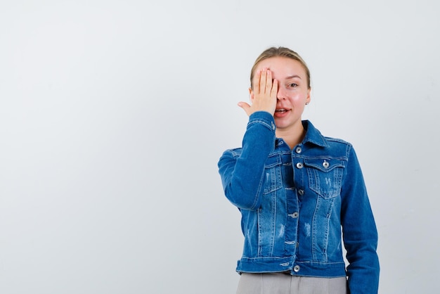 La mujer rubia se cubre el ojo con la mano en el fondo blanco