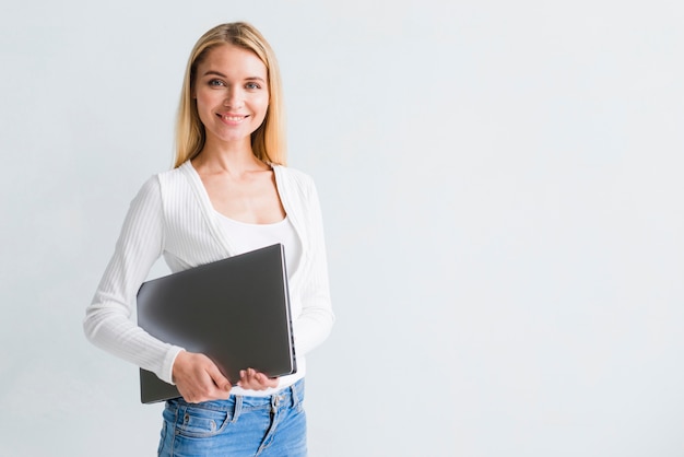 Mujer rubia delgada sonriente en pantalones vaqueros con la computadora portátil negra