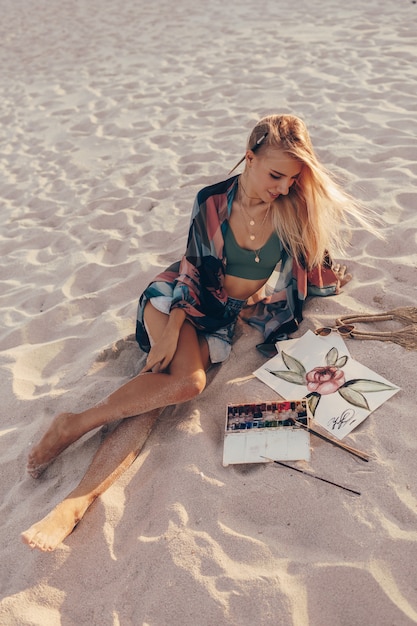 Mujer rubia dibujo acuarela flor con pincel en la playa