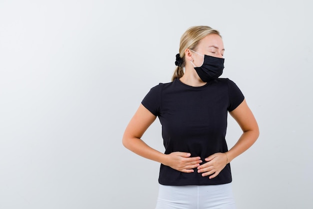 Mujer rubia con dolor de estómago en camiseta negra, pantalón blanco