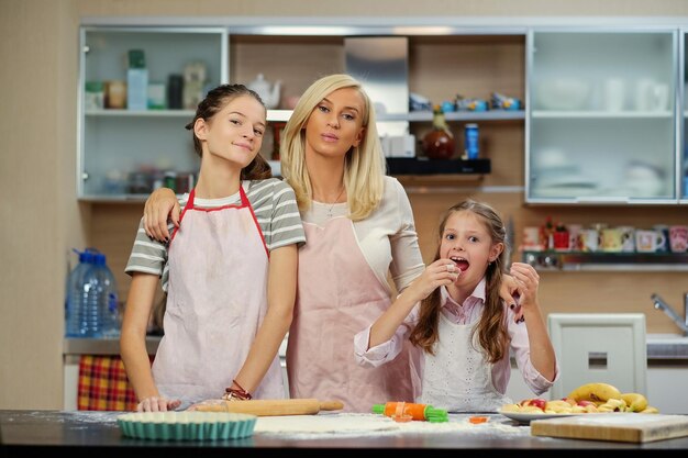 Mujer rubia y dos adolescentes que muestran cómo amasar en la cocina de la casa.