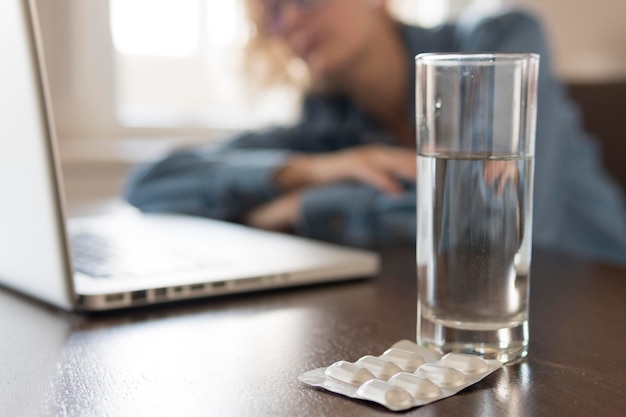 Mujer rubia durmiendo en la mesa de la cocina cerca de una computadora portátil y pastillas