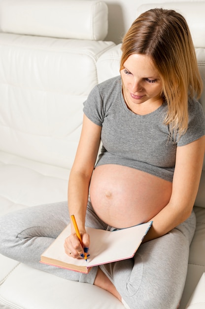 Mujer rubia embarazada escribiendo algo en un libro