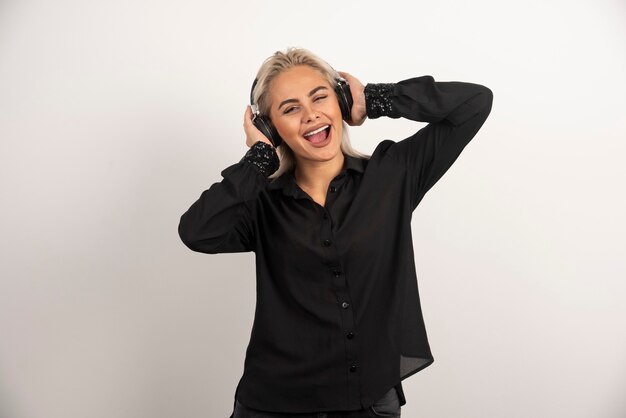 Mujer rubia escuchando la canción con auriculares sobre fondo blanco. Foto de alta calidad