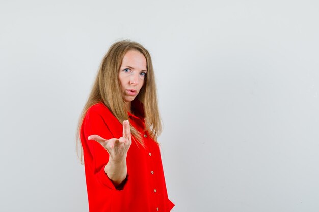 Mujer rubia estirando la mano en gesto de perplejidad en camisa roja