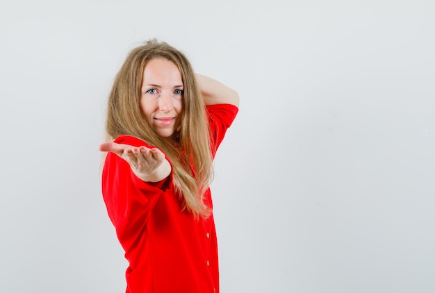 Mujer rubia estirando la mano y sonriendo con camisa roja