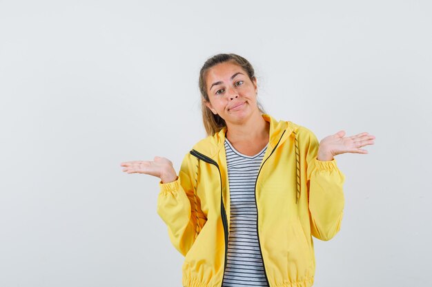 Mujer rubia estirando las manos de manera interrogante en chaqueta de bombardero amarilla y camisa a rayas y mirando desconcertado