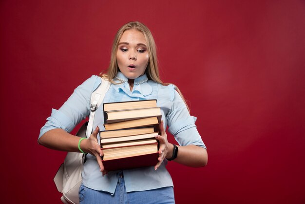 Mujer rubia estudiante sosteniendo una pila de libros y parece positiva.