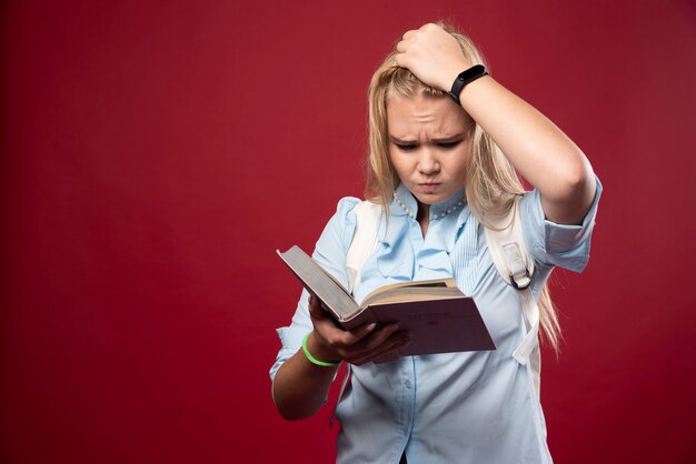 La mujer rubia estudiante sostiene sus libros y parece aterrorizada.