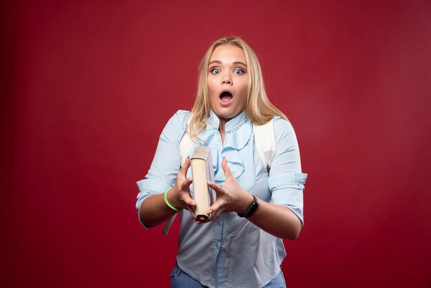 La mujer rubia estudiante sostiene sus libros y parece aterrorizada.