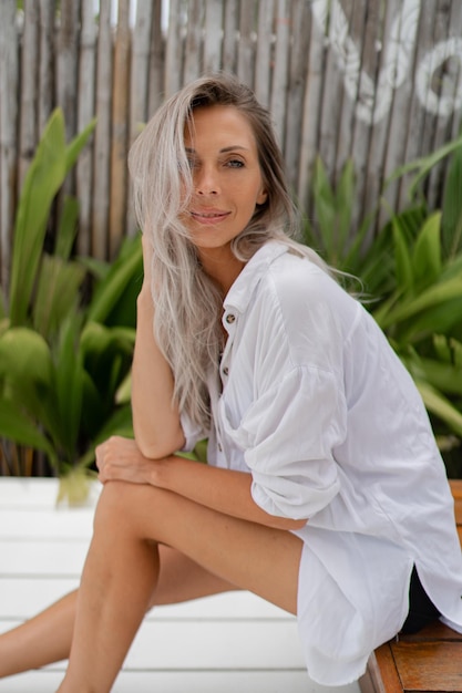 Foto gratuita mujer rubia feliz en blusa blanca posando en un resort tropical concepto de viaje y vacaciones