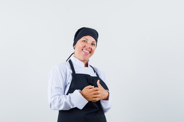 Mujer rubia frotándose las manos en uniforme de cocinero negro y luciendo bonita, vista frontal.
