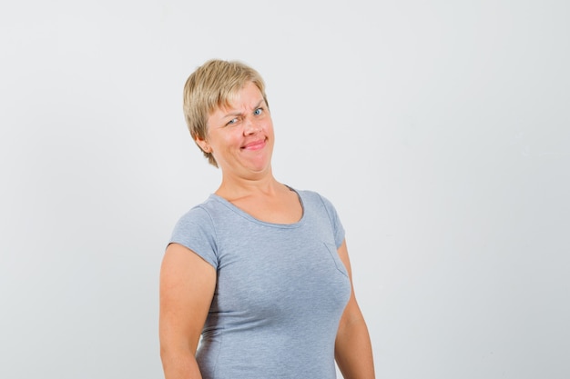 Mujer rubia frunciendo el ceño en una camiseta azul claro y mirando disgustado, vista frontal.