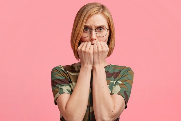 Mujer rubia con gafas redondas y camiseta de camuflaje