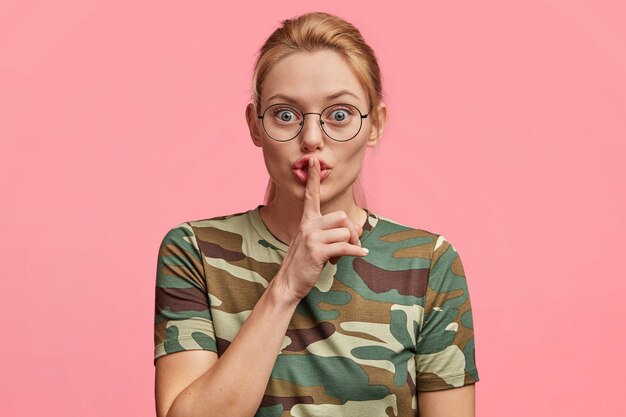 Mujer rubia con gafas redondas y camiseta de camuflaje