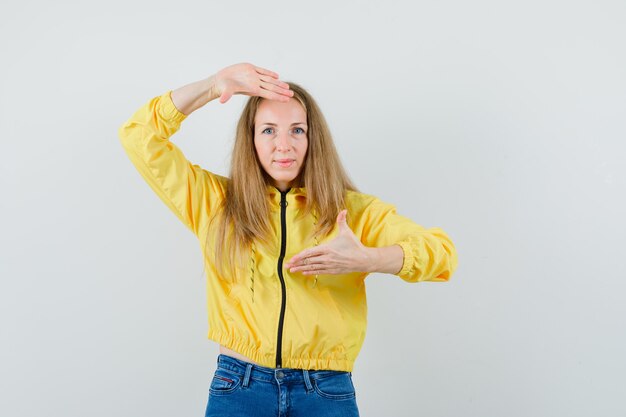 Mujer rubia haciendo gesto de marco en chaqueta, jeans y mirando alegre,