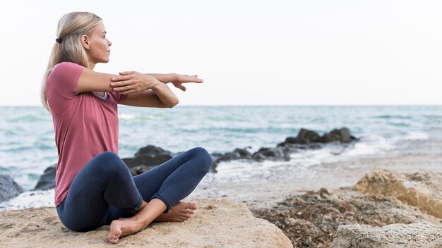 Mujer rubia haciendo yoga en la playa