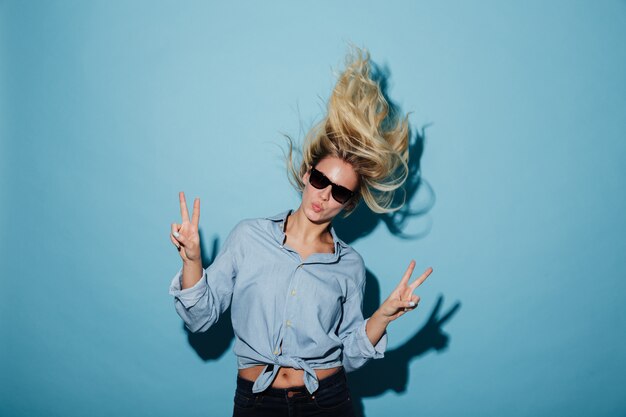 Mujer rubia inusual en camisa y gafas de sol mostrando gestos de paz