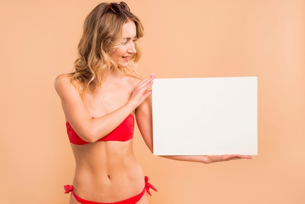 Foto gratuita mujer rubia joven en el bikini rojo que lleva a cabo al tablero en blanco