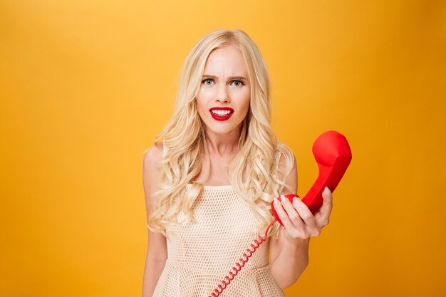 Mujer rubia joven confundida que sostiene el teléfono.