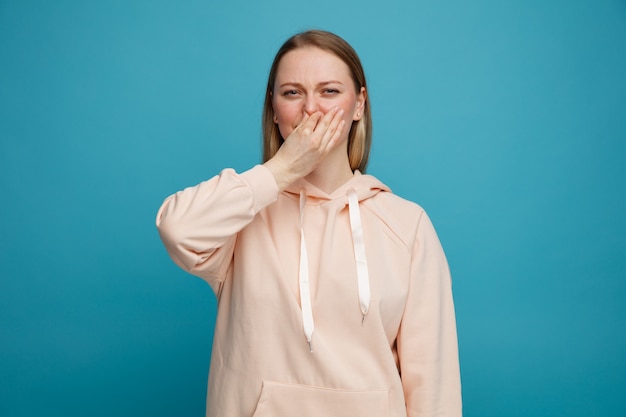 Mujer rubia joven disgustada haciendo gesto de mal olor