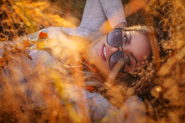 Mujer rubia joven en gafas de sol tumbado en la hierba dorada.