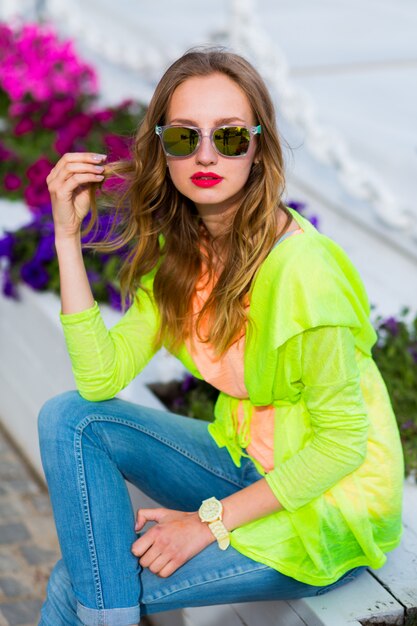 Mujer rubia joven inconformista con estilo en gafas de sol con cóctel posando al aire libre