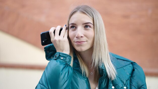 Mujer rubia joven que escucha el mensaje de voz en la calle