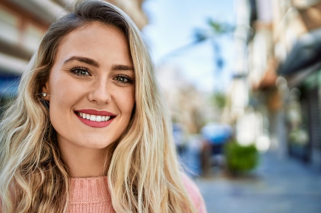 Mujer rubia joven que sonríe en la ciudad