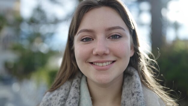 Mujer rubia joven sonriendo confiada de pie en el parque