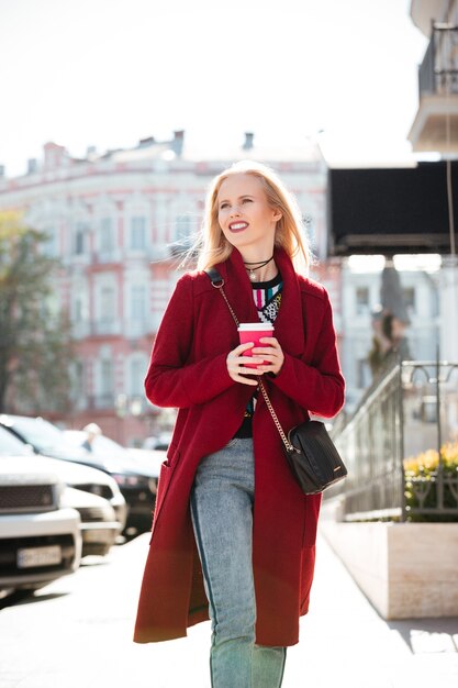 Mujer rubia joven sonriente de la moda que camina al aire libre