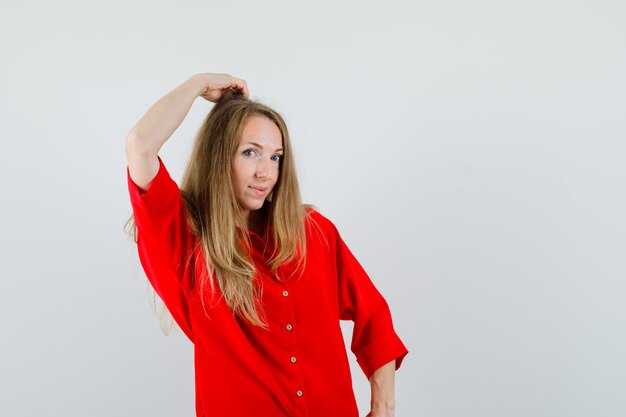 Mujer rubia con la mano en la cabeza con camisa roja y un aspecto fascinante.