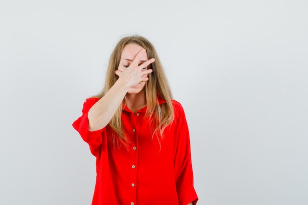 Mujer rubia con la mano en la cara con camisa roja y aspecto fatigado.