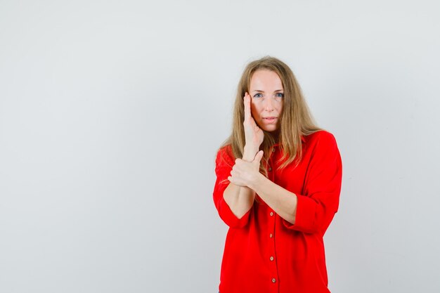 Mujer rubia con la mano en la mejilla con camisa roja y un aspecto impresionante.