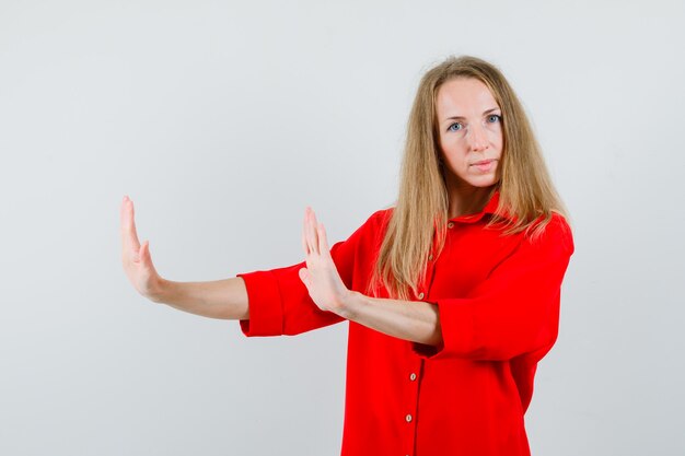 Mujer rubia manteniendo las manos de manera preventiva en camisa roja y mirando con cuidado,