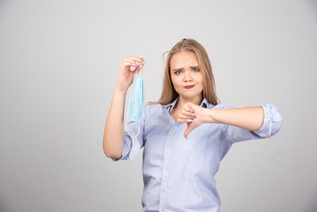 mujer rubia con mascarilla médica mostrando el pulgar hacia abajo.