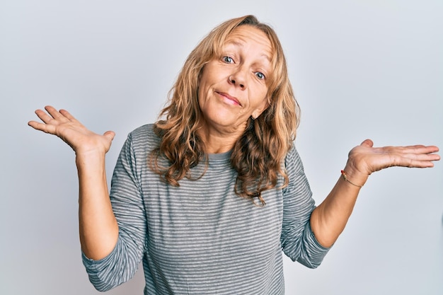 Foto gratuita mujer rubia de mediana edad con ropa informal sin idea y confundida con los brazos abiertos sin idea y cara dudosa