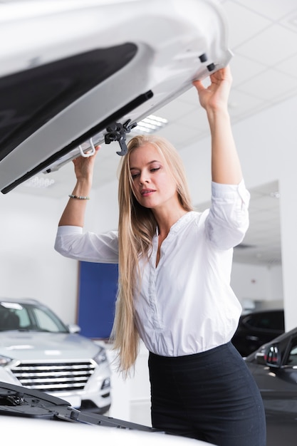 Mujer rubia mirando debajo del capó del coche